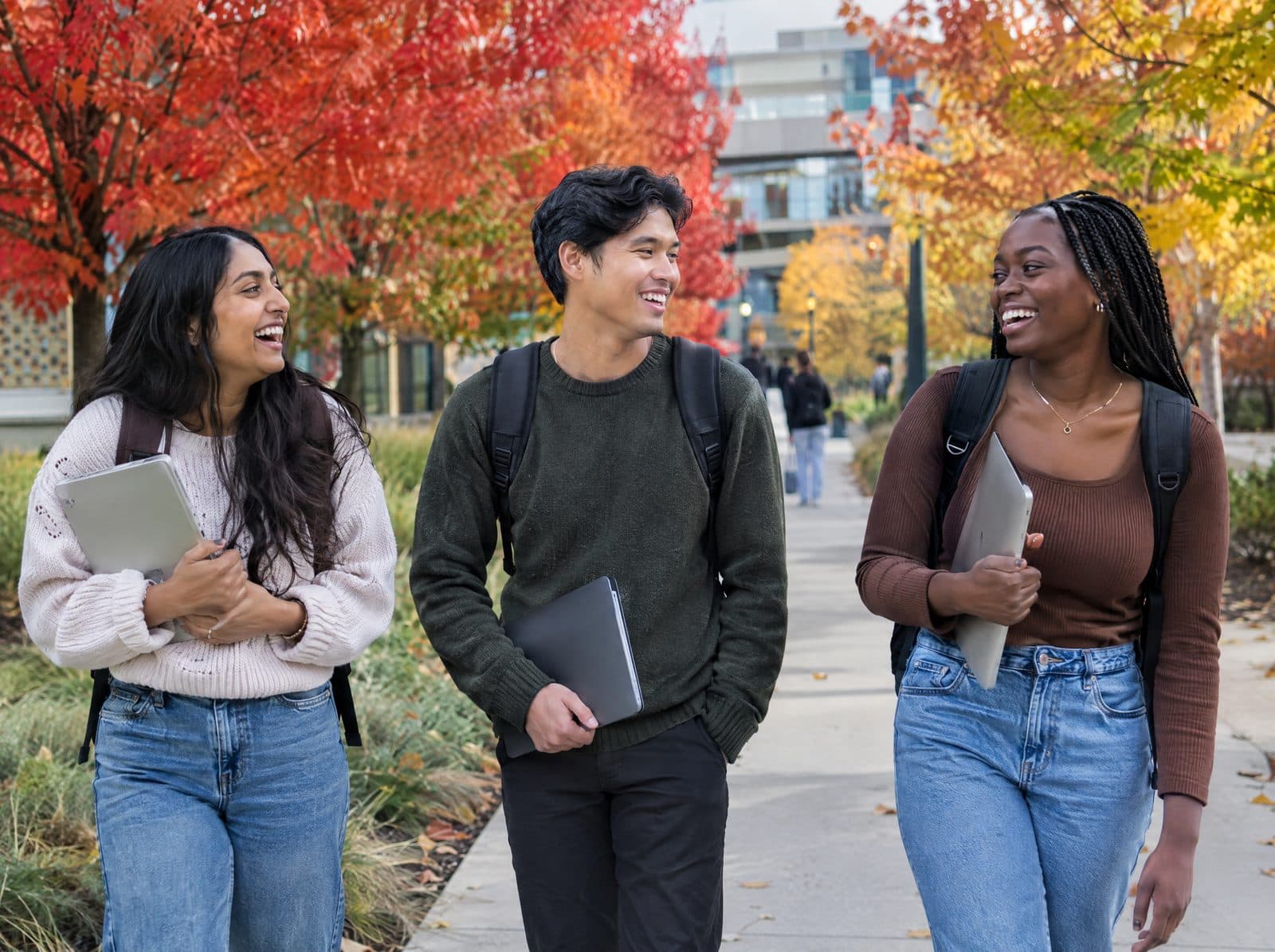 Three international students laughing together on a Canadian campus in autumn